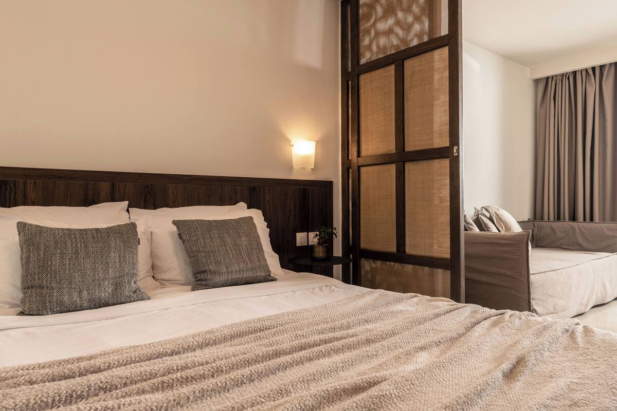 Habitación de hotel con cama, mesita de noche, lámpara de pared y vistas a través de una ventana con cortinas.