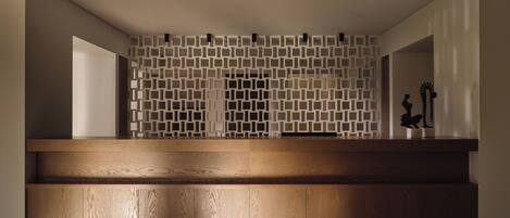 A reception desk with a wooden finish, a geometric patterned wall, and a minimalist design.