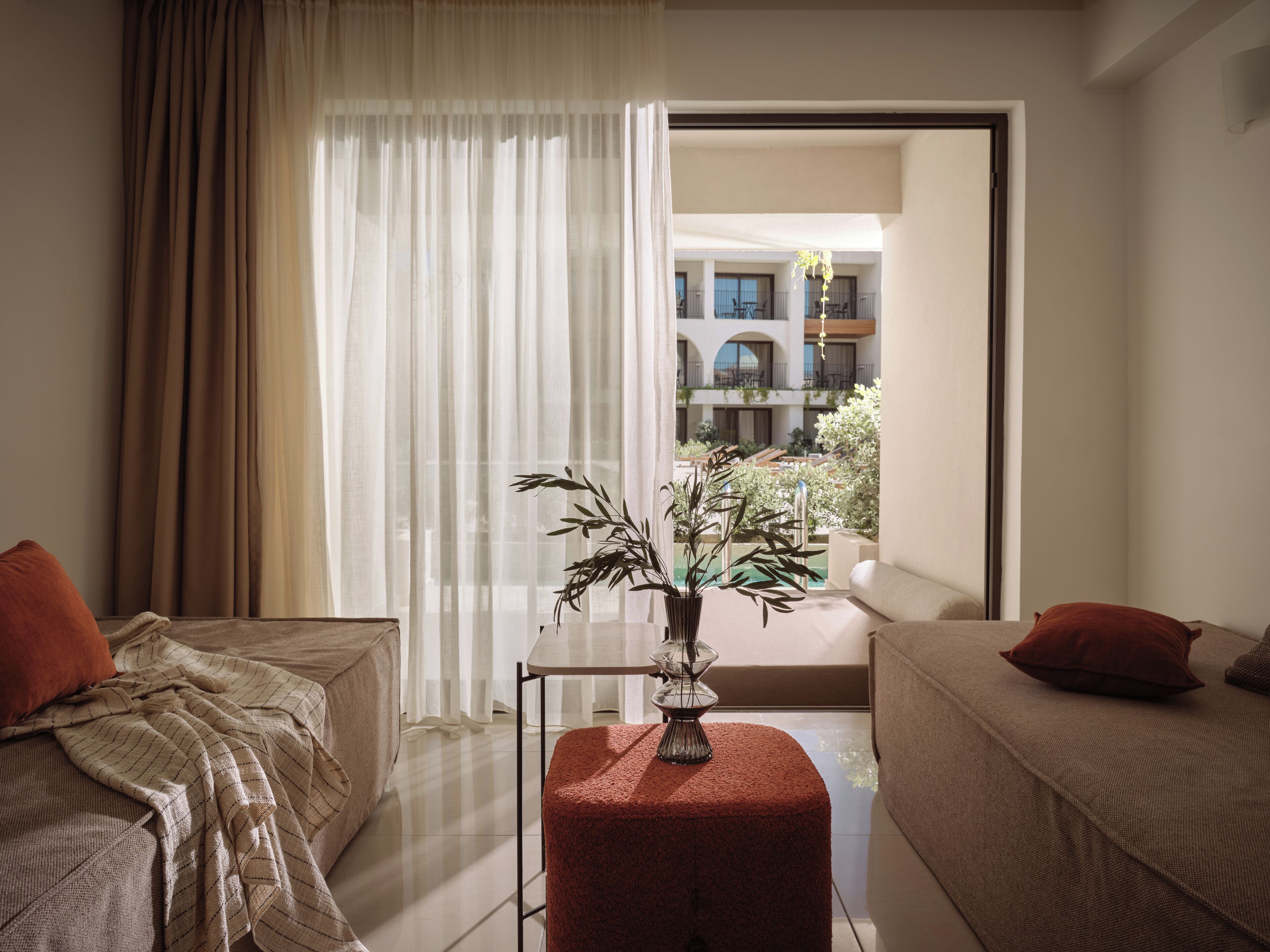 Habitación de hotel con dos camas, una planta en maceta y vista a un patio.