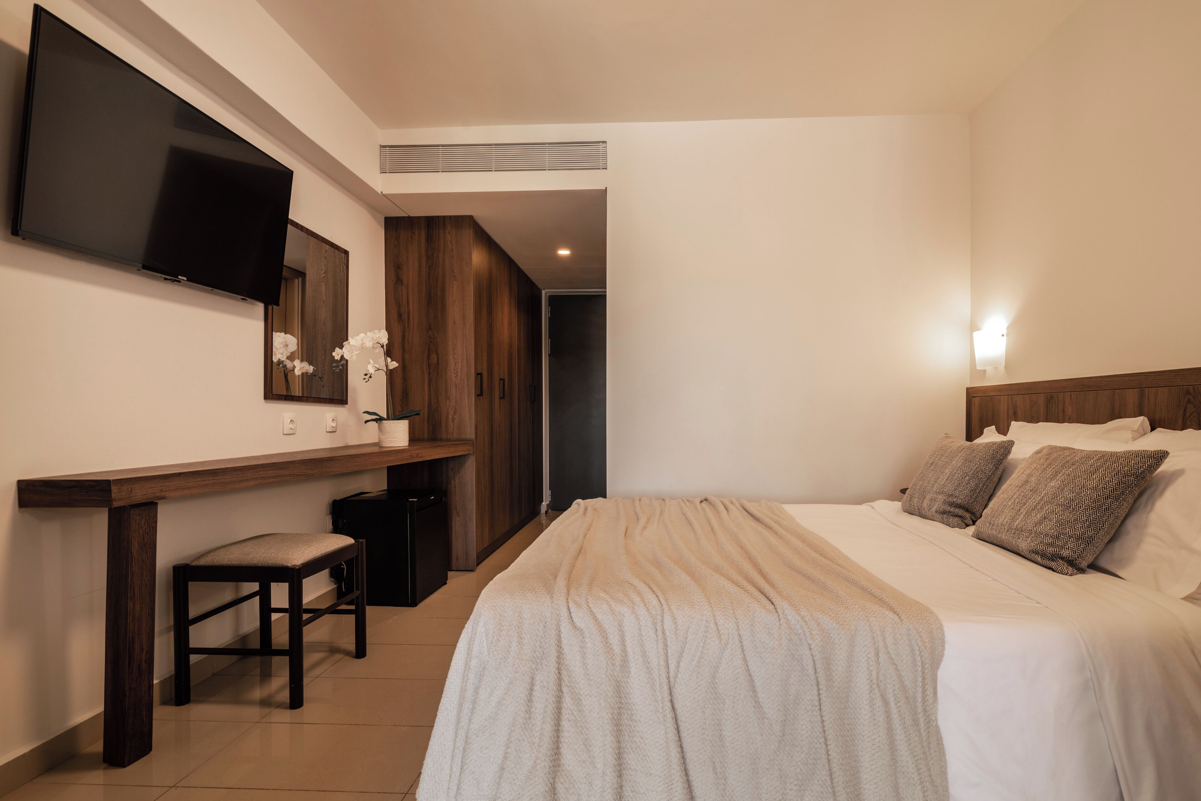 A hotel room with a bed, a desk, a chair, a TV mounted on the wall, and a mirror.