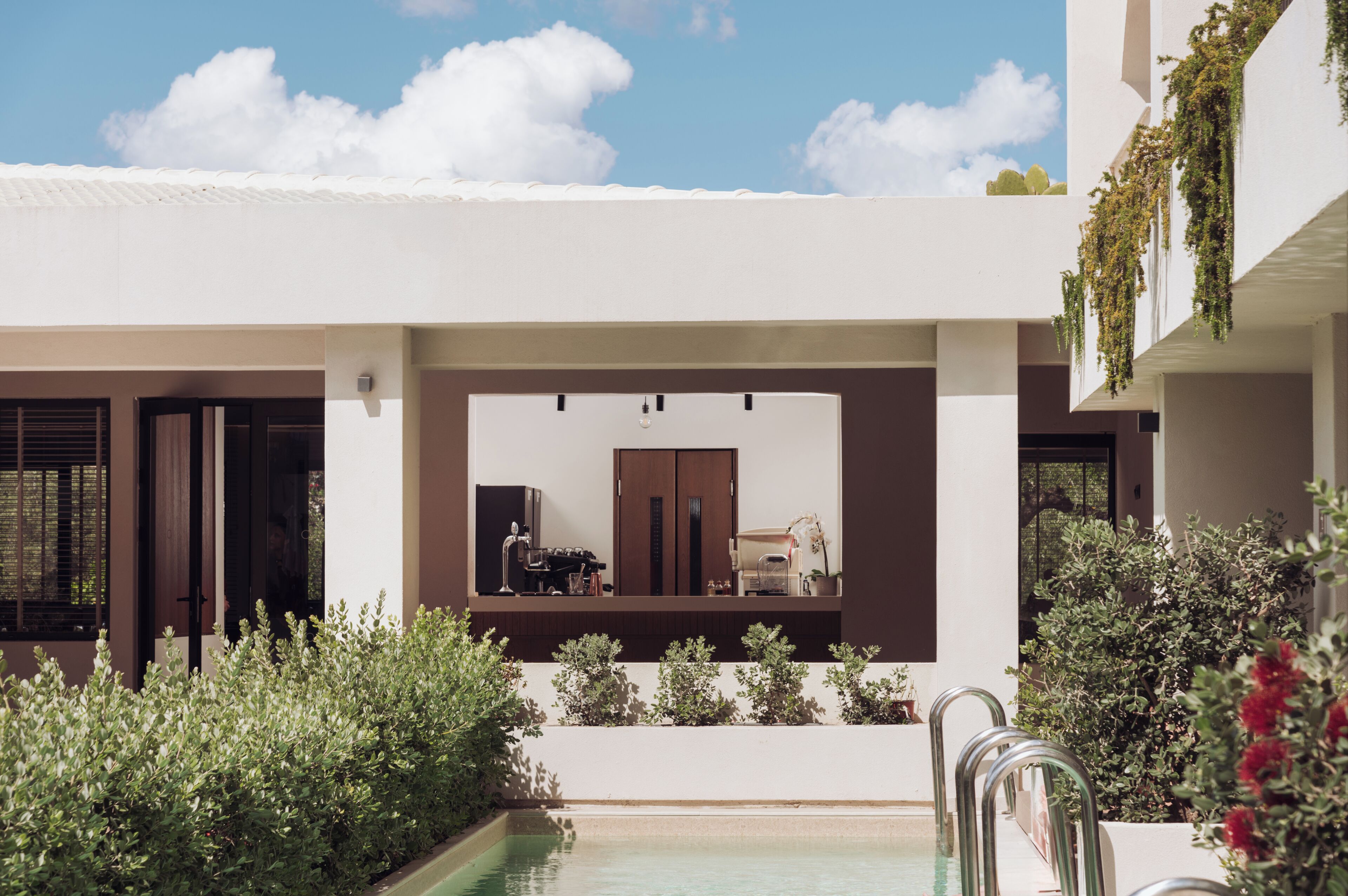 A modern building with a pool, outdoor seating, and greenery.