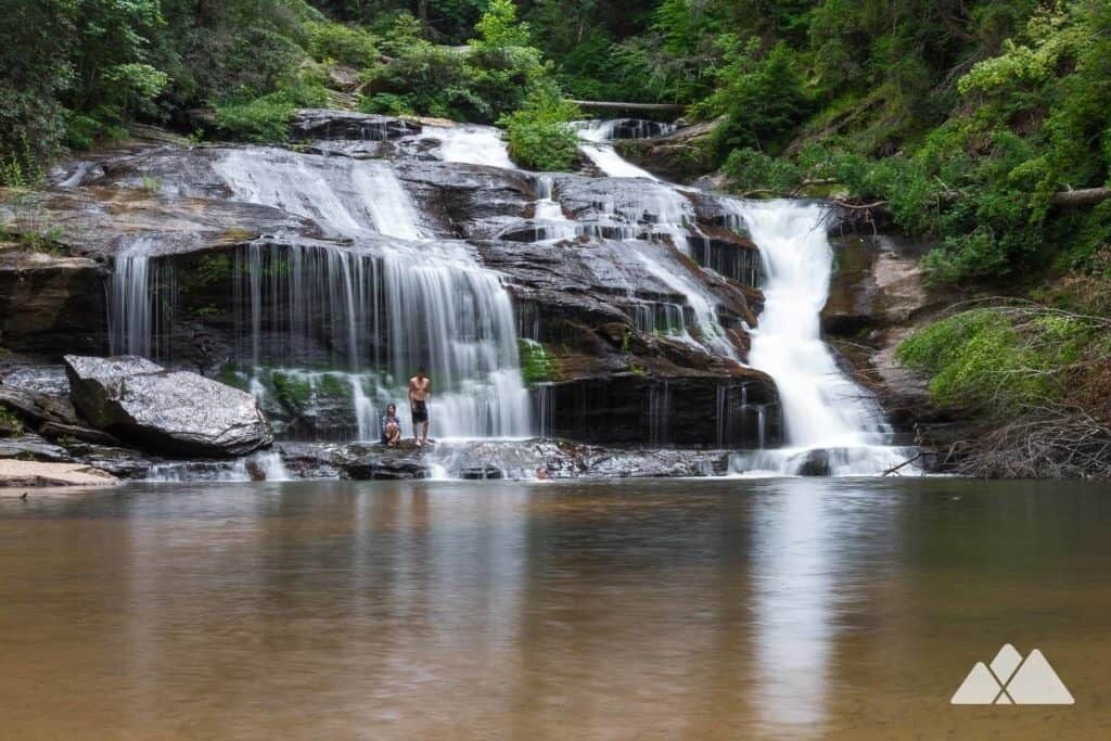 A waterfall cascading over rocks into a calm pool surrounded by lush greenery.