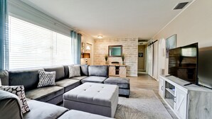 A modern living room with a sectional sofa, ottomans, a fireplace, and a TV. - Beautiful 3 bdrm Private home with HEATED pool 5 mi from Anna Maria Island!! (Bradenton)
