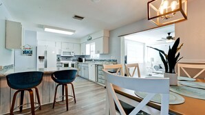 A modern kitchen with white cabinets, a microwave, and a stove. There are two bar stools and a dining table with chairs. - Beautiful 3 bdrm Private home with HEATED pool 5 mi from Anna Maria Island!! (Bradenton)