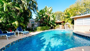 A swimming pool with a tiled edge, surrounded by lush greenery and palm trees. - Beautiful 3 bdrm Private home with HEATED pool 5 mi from Anna Maria Island!! (Bradenton)