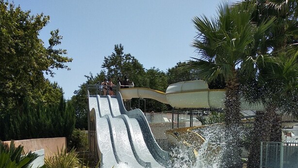 A water slide with a pool at the bottom, surrounded by greenery and a clear sky. - Your vacation with peace of mind! (Agde)