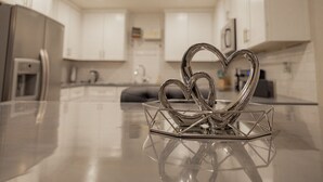 Una cucina moderna con mobili bianchi, un frigorifero in acciaio inossidabile e un oggetto decorativo a forma di cuore sul piano di lavoro.