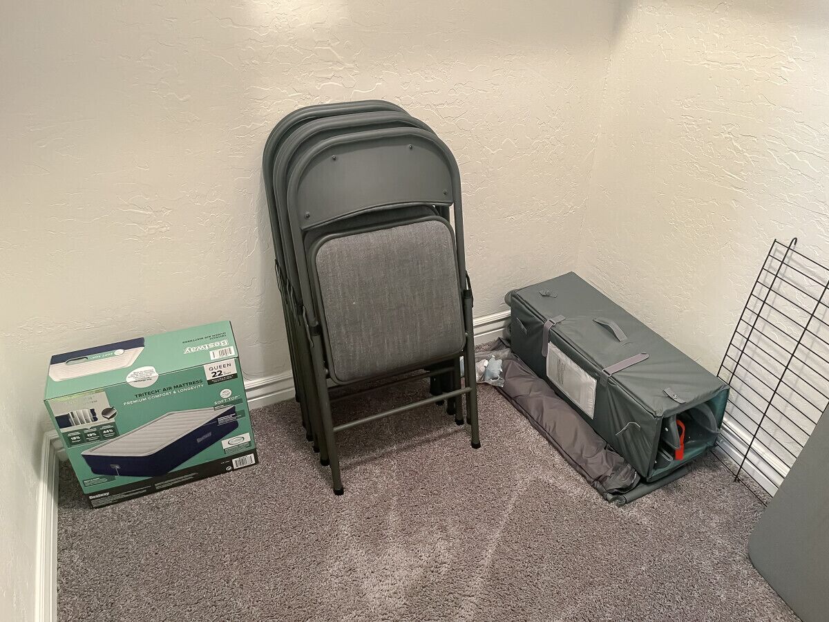 Une pièce avec un matelas gonflable gris, une boîte verte et une valise grise.