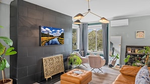 A modern living room with a large TV, comfortable seating, and a view of the outdoors. - Casa Ballard - Entire Renovated Home with Patio, Deck & Private Basement (Seattle)