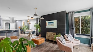 A modern living room with a dining area, a black accent wall, and a large window with curtains. - Casa Ballard - Entire Renovated Home with Patio, Deck & Private Basement (Seattle)