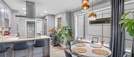A modern kitchen with a central island, bar stools, a dining table with placemats, and pendant lighting.