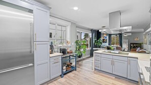 A modern kitchen with grey cabinets, a stainless steel refrigerator, and a central island. - Casa Ballard - Entire Renovated Home with Patio, Deck & Private Basement (Seattle)