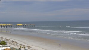 A beach with a pier extending into the ocean, a sandy shore, and a few people walking. - 3BR/3BA Direct Oceanfront Condo - Magnificent Panoramic View! (daytona beach shores)