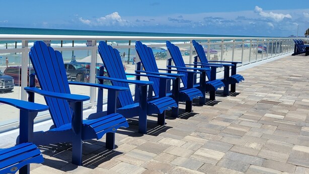 A row of blue Adirondack chairs on a stone deck overlooking the beach. - 3BR/3BA Direct Oceanfront Condo - Magnificent Panoramic View! (daytona beach shores)