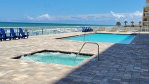 A swimming pool with a view of the ocean, surrounded by lounge chairs and a tiled deck. - 3BR/3BA Direct Oceanfront Condo - Magnificent Panoramic View! (daytona beach shores)