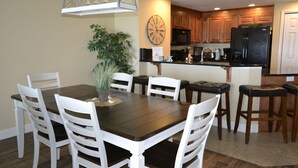 A dining area with a wooden table and white chairs, a potted plant, and a kitchen in the background. - 3BR/3BA Direct Oceanfront Condo - Magnificent Panoramic View! (daytona beach shores)