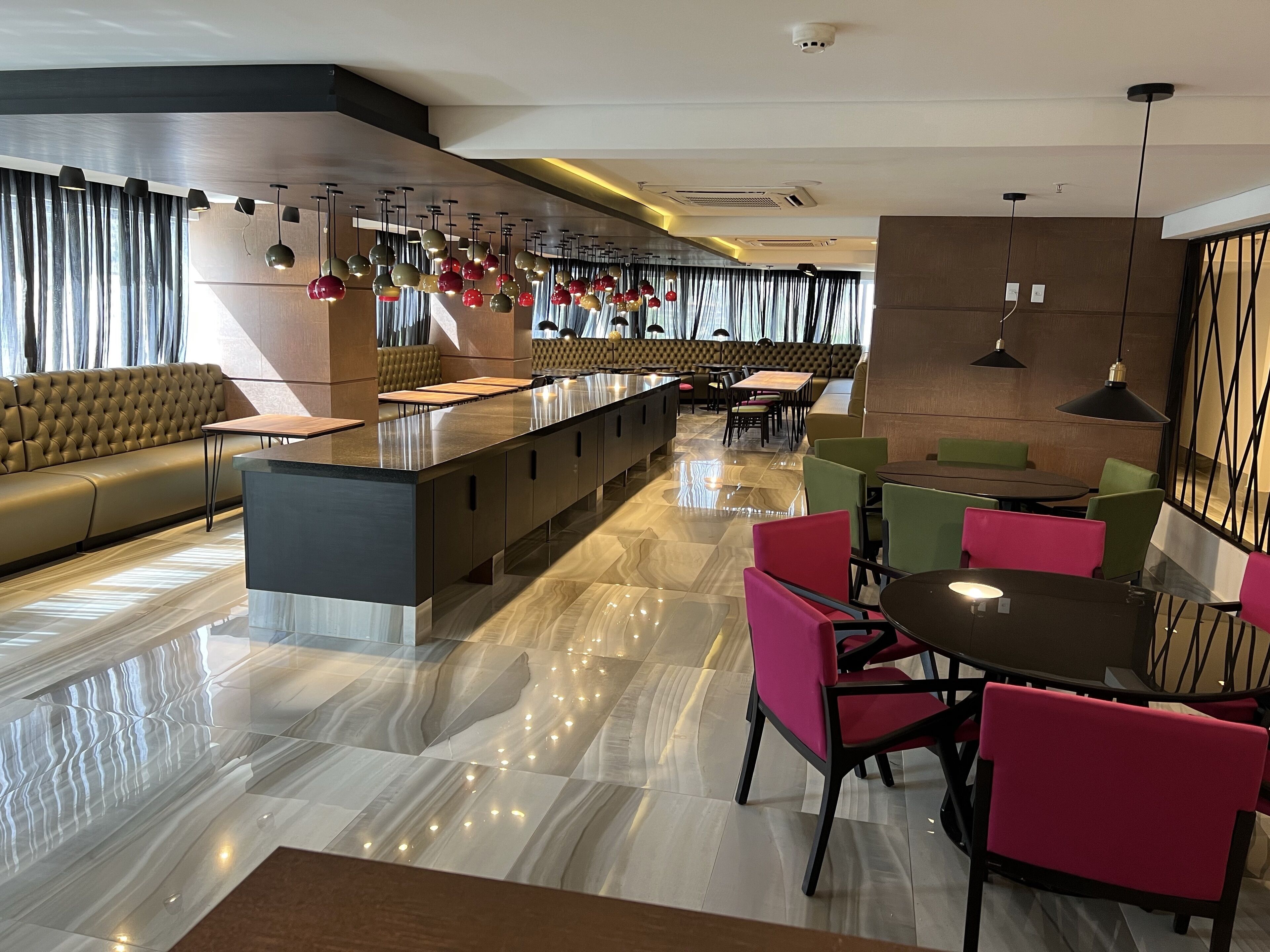 A modern hotel lobby with a central bar, seating areas, and a mix of tables and chairs.