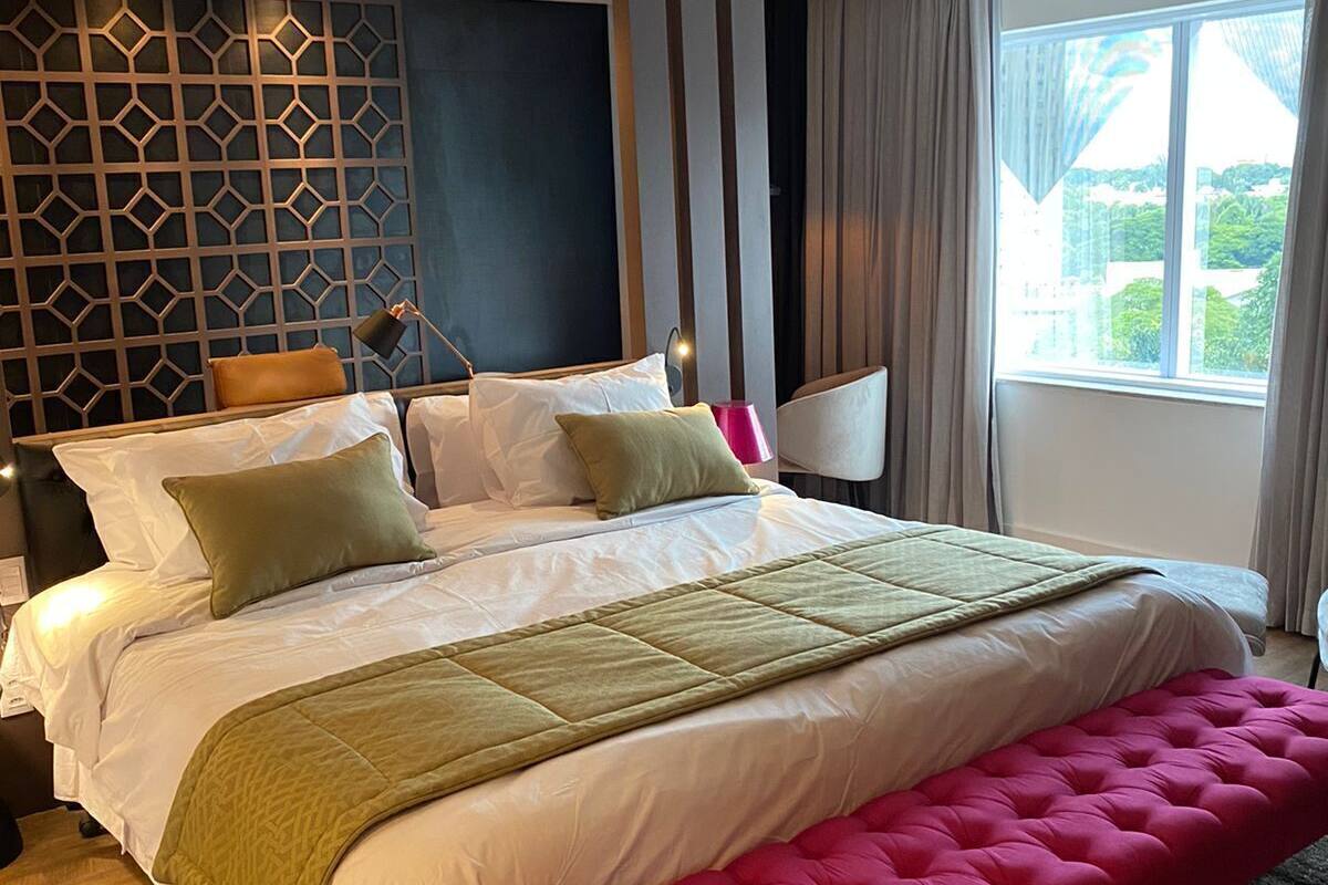 Camera d'hotel moderna con un letto grande, una panca, vista sulla città e un design geometrico alla parete.