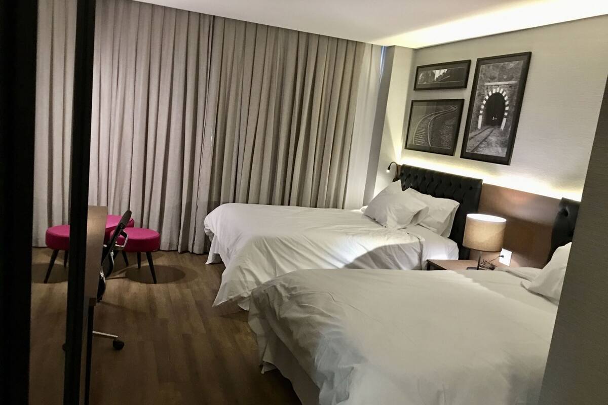 Camera d'albergo con due letti, una scrivania, una sedia e una parete decorata con quadri.