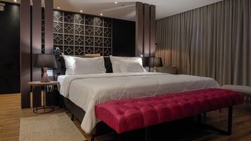 A modern hotel room with a large bed, a red bench, two bedside tables with lamps, and a geometric wall design.