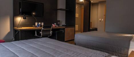 A hotel room with two beds, a desk with a chair, a TV, and a wardrobe.