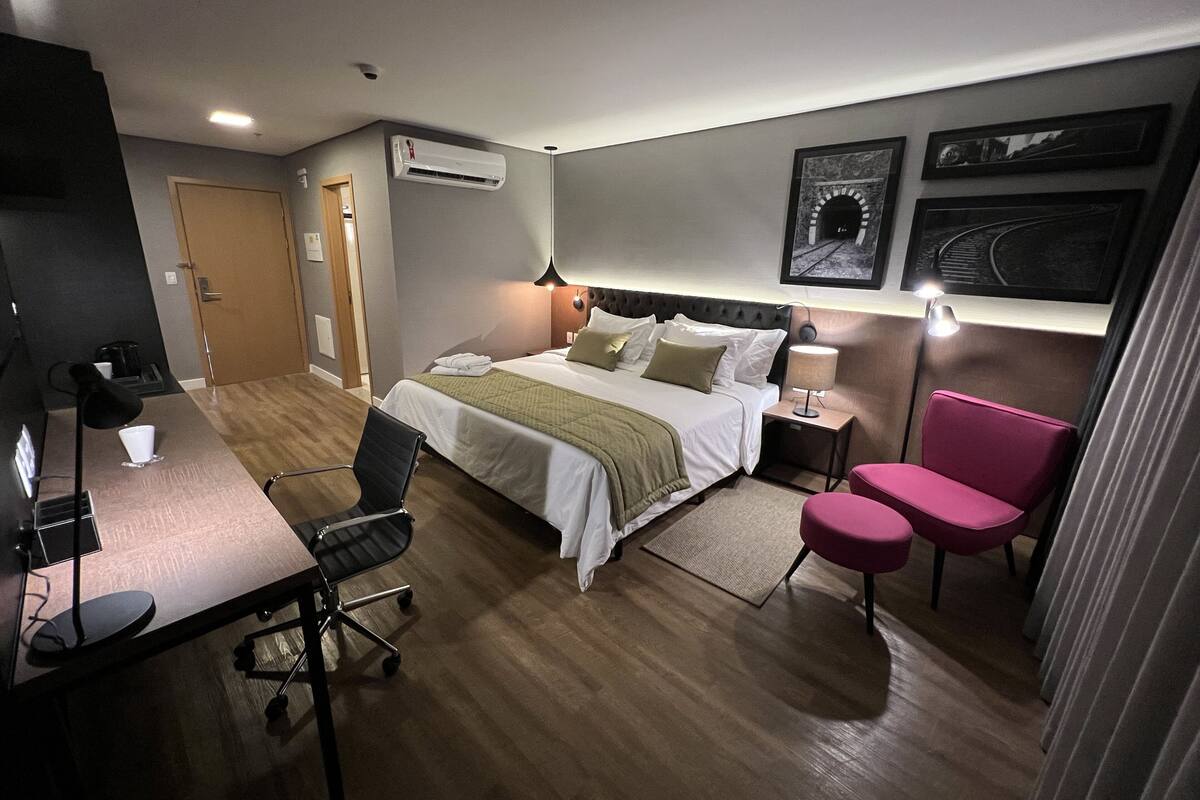 Una camera d'albergo con un letto, una scrivania, una sedia e un comodino con una lampada.