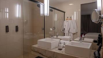 Un baño moderno con cabina de ducha de vidrio, dos lavamanos y un espejo grande.
