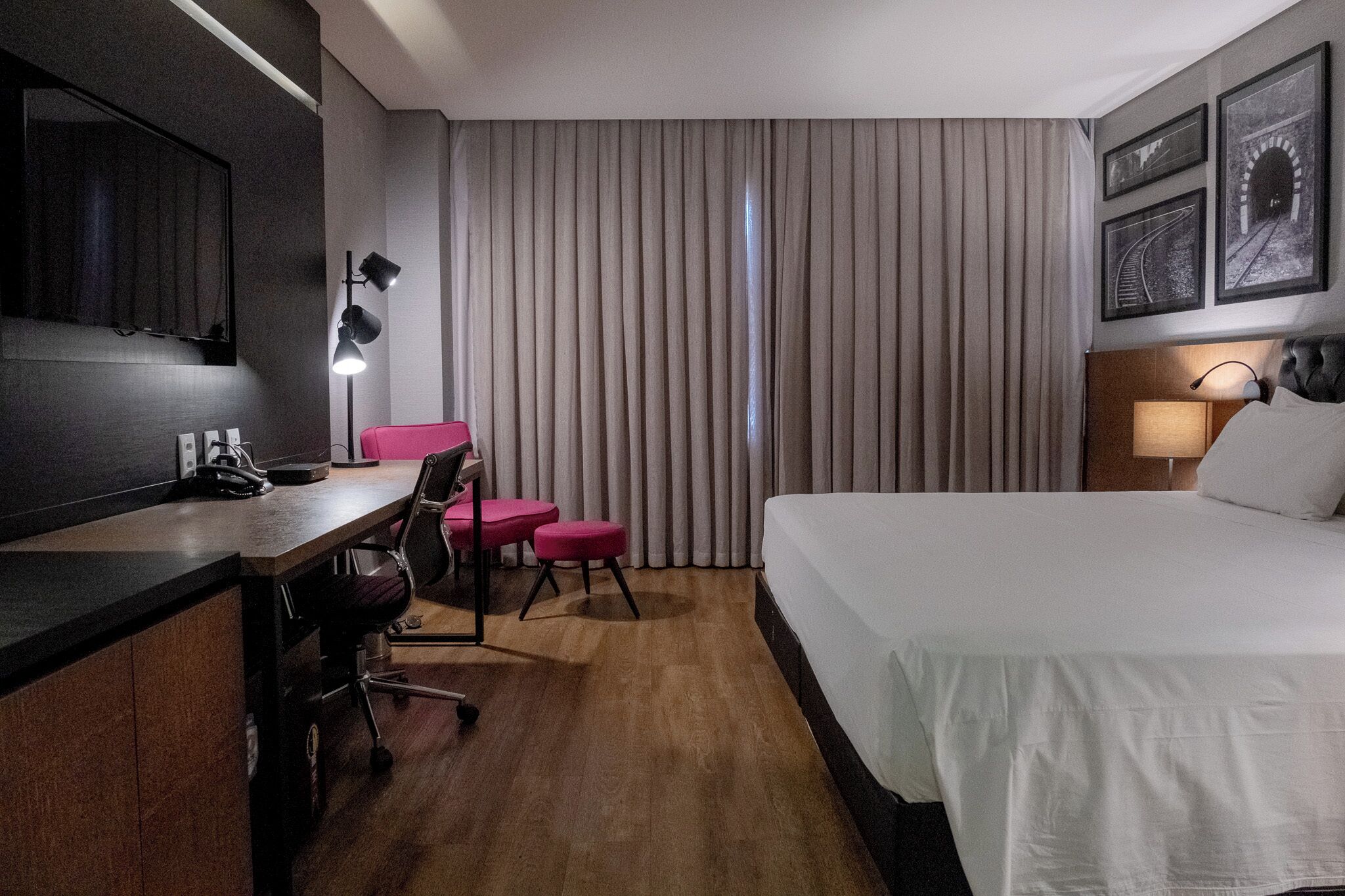 Habitación de hotel con cama, escritorio, silla y un ventanal con cortinas.