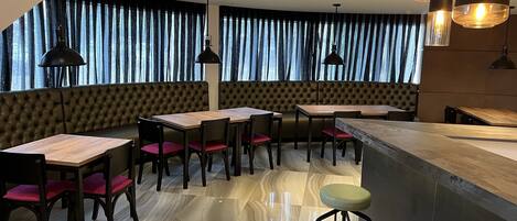 Un restaurante moderno con techo alto, asientos tipo banca de cuero negro, mesas de madera e iluminación colgante negra.