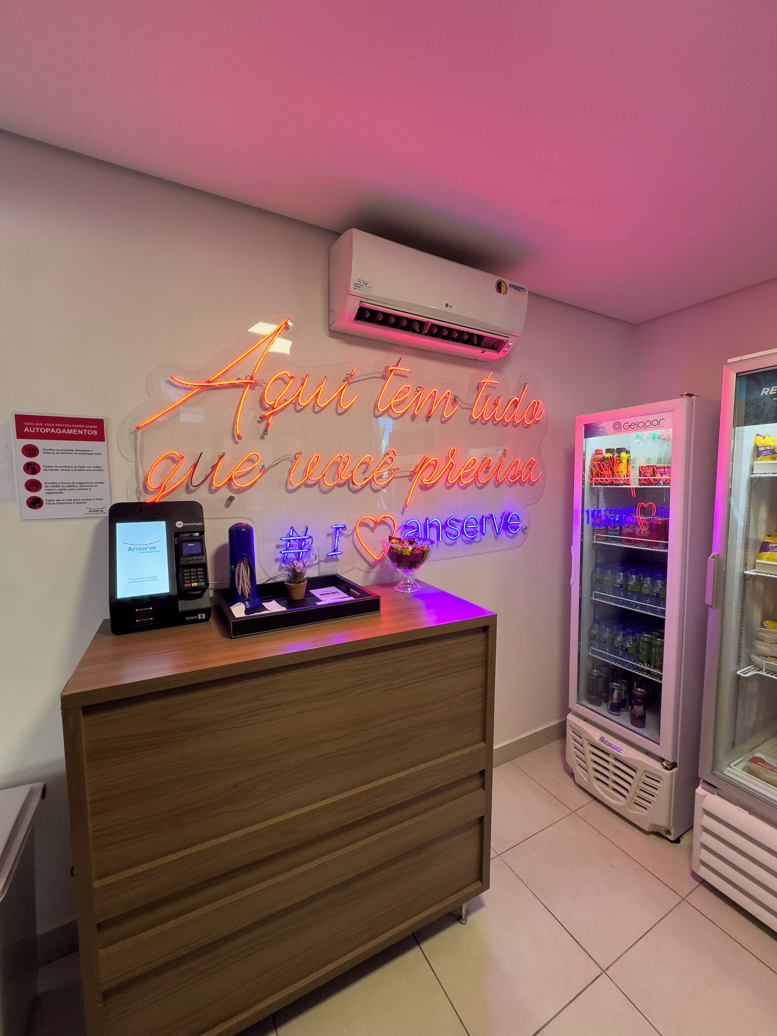 A reception desk with a neon sign, a self-service kiosk, and a refrigerator.