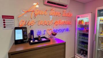 A reception desk with a neon sign, a self-service kiosk, and a refrigerator.