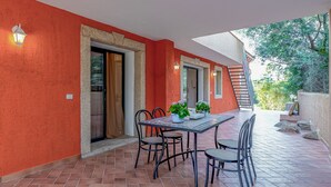 An outdoor patio with a table and chairs, a stone wall, and a staircase leading to a covered area. - Domos Pintadas Apt. 3 Porto Rotondo (Olbia)