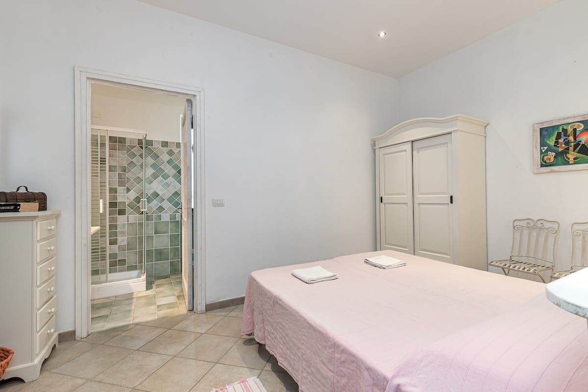 A bedroom with a bed, a wardrobe, a bathroom with a shower, and a tiled wall.