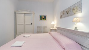 A bedroom with a bed, a wardrobe, two chairs, a nightstand with a lamp, and a wall-mounted shelf. - Domos Pintadas Apt. 3 Porto Rotondo (Olbia)