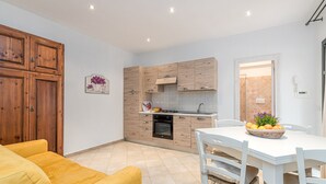 A modern kitchen with wooden cabinets, a dining table with chairs, and a yellow sofa. - Domos Pintadas Apt. 3 Porto Rotondo (Olbia)