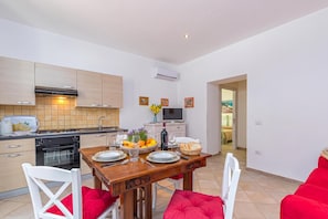 Une cuisine moderne avec un coin repas, comprenant une table en bois dressée pour deux personnes, un téléviseur et une vue sur la salle à manger.