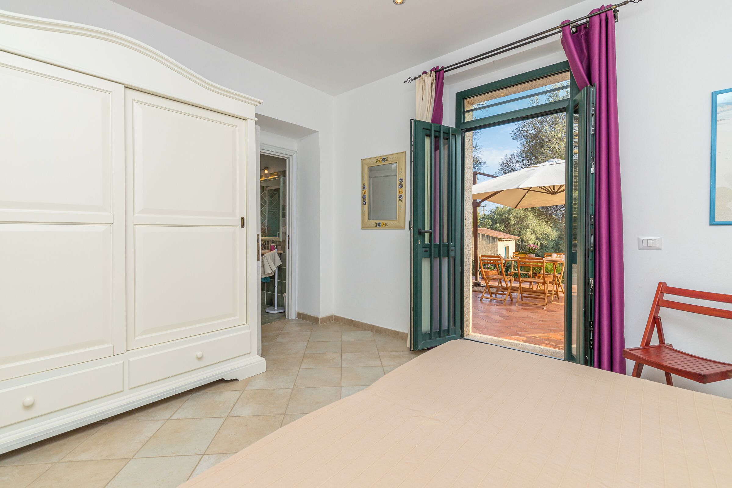 A bedroom with a large wardrobe, a bed, and a view of an outdoor patio with tables and chairs.