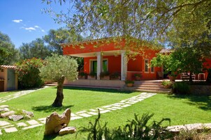 Un edificio rojo con columnas, un camino de piedra y un árbol en primer plano.