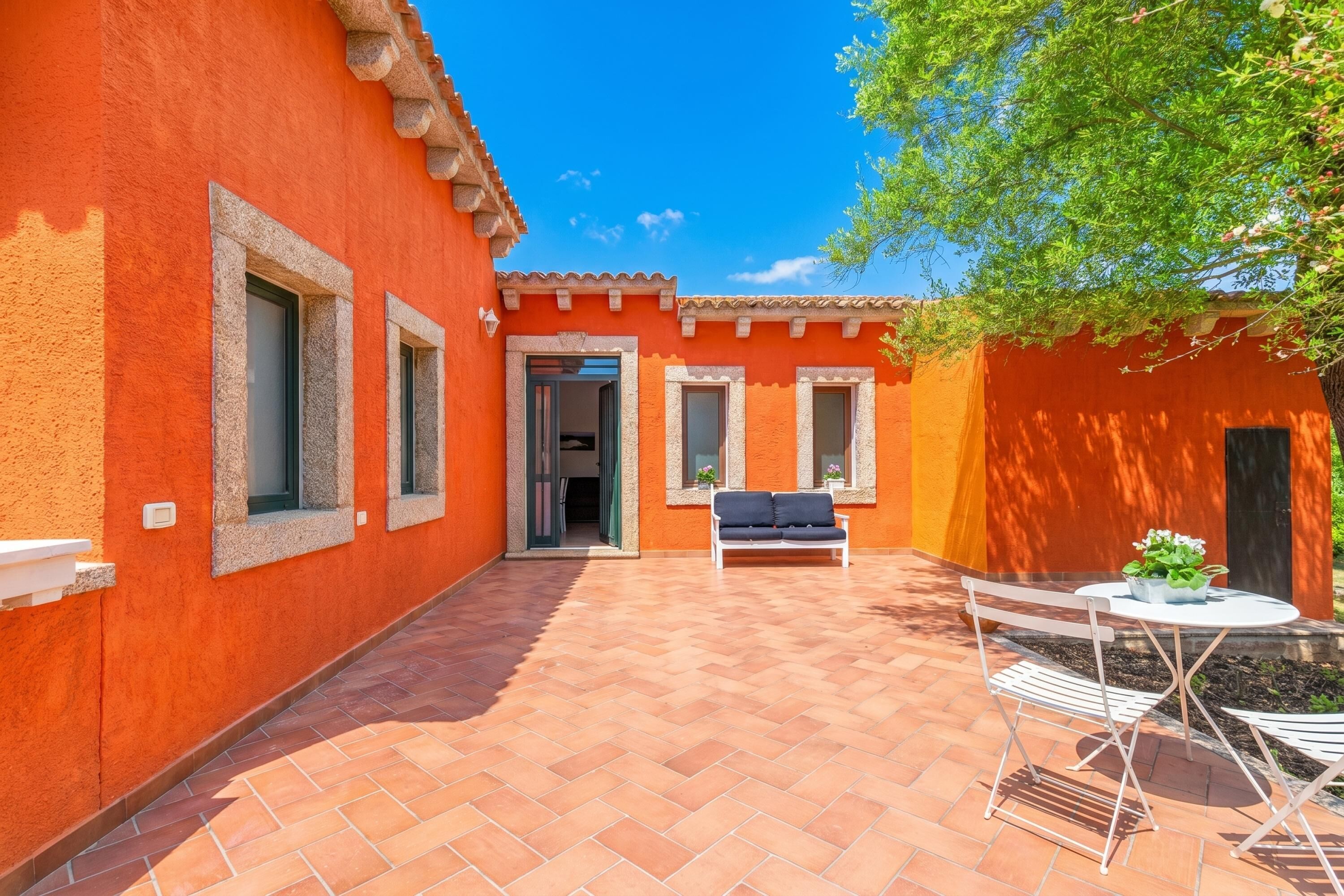 A courtyard with a patio, a white bench, and a table with a potted plant.