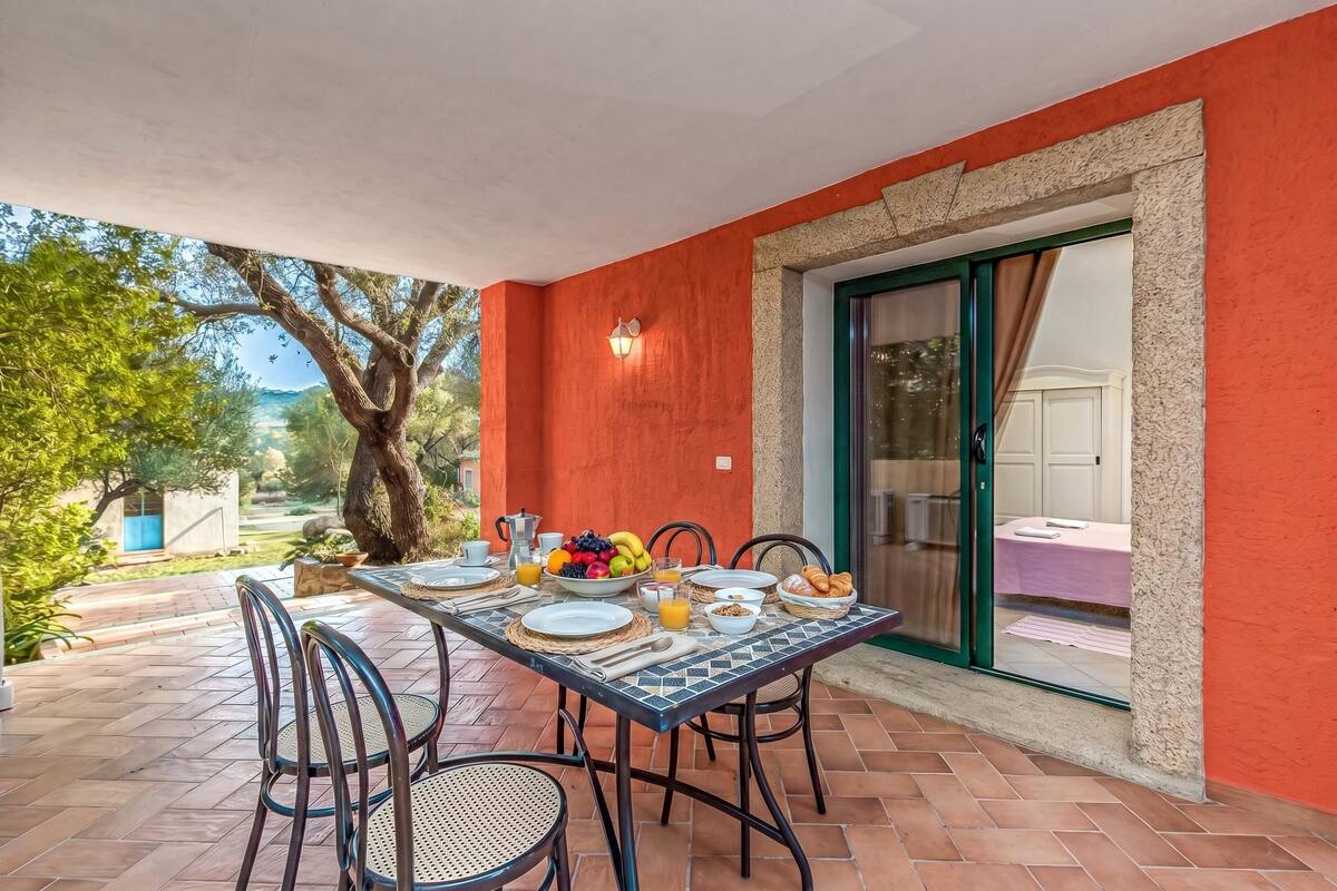 An outdoor dining area with a table set for breakfast, surrounded by chairs, and a view of the garden.