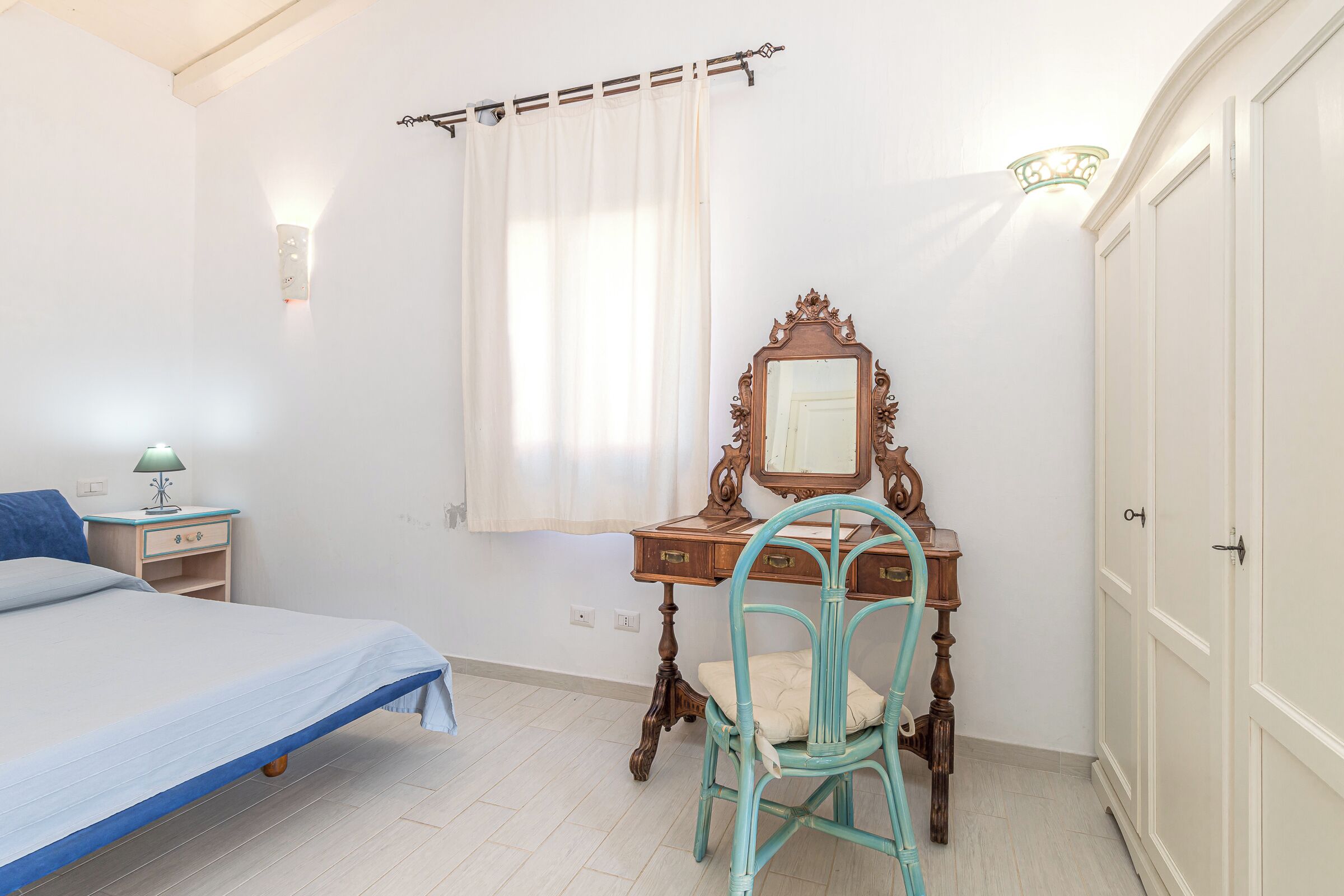 A bedroom with a bed, a dresser with a mirror, a chair, a nightstand, and a window with curtains.