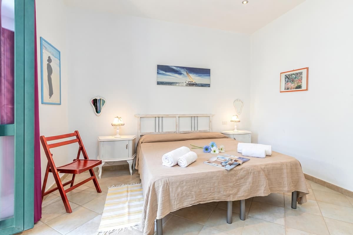 A bedroom with a bed, two bedside tables, a chair, and a painting on the wall.