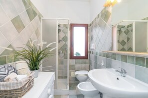 A bathroom with a shower, toilet, and sink, featuring a tiled backsplash and a window.