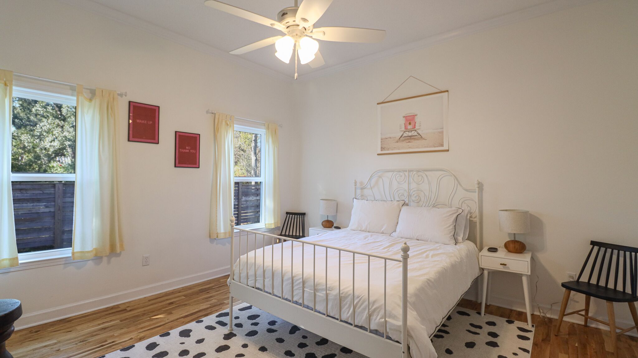 A bedroom with a bed, two bedside tables, a chair, a ceiling fan, and a window with curtains.