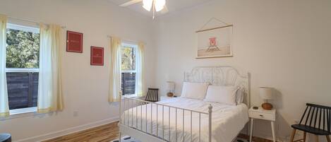 A bedroom with a bed, two bedside tables, a chair, a ceiling fan, and a window with curtains.