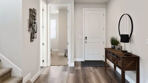A hallway with a wooden floor, a white door, and a wooden console table with a lamp and a welcome sign. - Large 5 Bed 5 Bath Home w/Private Hot Tub (Washington)