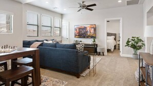 A spacious living room with a blue sofa, a wooden coffee table, and a chessboard. There is a ceiling fan, a painting on the wall, and a door leading to another room. - Large 5 Bed 5 Bath Home w/Private Hot Tub (Washington)