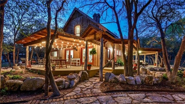 Eine rustikale Holzhütte mit überdachter Veranda, einem Kiesweg und umliegenden Bäumen.