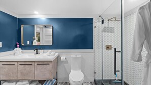 Une salle de bain moderne avec un mur d’accent bleu, un lavabo blanc et une douche en verre.