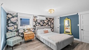 Ein Schlafzimmer mit einem Bett, einem Nachttisch, einem Sessel, einem Spiegel und einem Fenster.